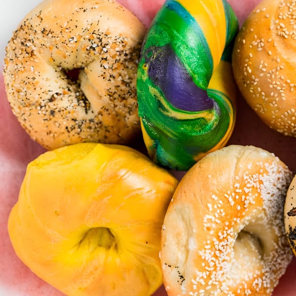Assortment of bagels, including everything, sesame, plain, and a colorful rainbow bagel.