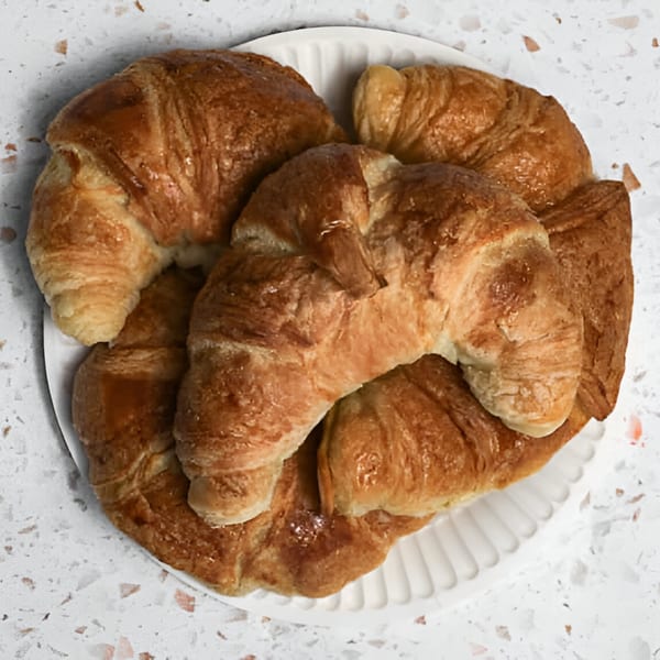 A white plate filled with several golden-brown, flaky croissants on a speckled white surface.